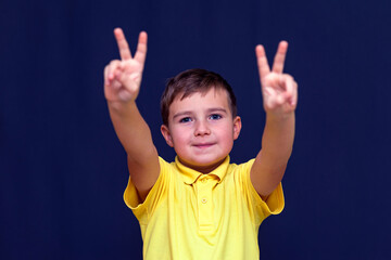 boy with fingers shows peace or victory sign on blue studio background