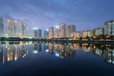 Fototapeta  - Buildings with reflections on lake at twilight at Thanh Xuan park. Hanoi cityscape at twilight period