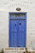 Niebieskie drzwi w białej ścianie greckiego domu na wyspie Amorgos