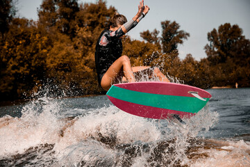 Wall Mural - young energetic woman skillfully jumping over the wave on surf style wakeboard