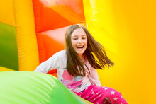 Happy Little Girl Having Lots Of Fun On A Jumping Castle During Sliding.
