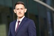 © Евгений Шемякин - Portrait of young serious businessman in formal suit with jacket and tie standing outdoors office business building, looking at camera with confident look