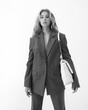 © Dmitry Tsvetkov - High fashion body length portrait of young beautiful female blonde model in classic gray male suit. Vogue style. Girl with blue eye arrows standing on white background and holding quilted handbag