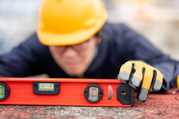 Asian maintenance worker man holding red aluminium spirit level tool or bubble levels at construction site. Equipment for civil engineering project