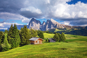 Wall Mural - Famous Alpe di Siusi - Seiser Alm with Sassolungo - Langkofel mountain group in background at sunset. Wooden chalets in Dolomites, Trentino Alto Adige region, South Tyrol, Italy