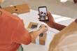 © AnnaStills - Close-up of man making photo of parcel on mobile phone while woman decorating the box