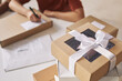 © AnnaStills - Close-up of parcel packed in cardboard box with ribbon on the table with woman working in the background