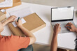 © AnnaStills - Close-up of man working online on laptop at the table with woman sitting near by him and writing address on the parcel