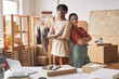 © AnnaStills - Portrait of young people standing back to back and smiling at camera while working with parcels in warehouse