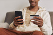 © AnnaStills - Close-up of African man holding mobile phone and credit card and paying for bills online sitting at home