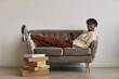 © AnnaStills - Happy African man lying on sofa with stacks of parcels on the floor and smiling at camera while buying purchases online on the phone