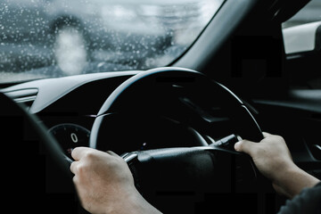 The hand of a man driving on the road on a rainy day. hands of a man with car steering wheel is ready on the move in the modern life style.