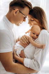 Beautiful parents with newborn baby girl, loving mom hold little daughter in arms, caring husband gently hug adorable wife, smiling, enjoy tender family moments, parenting concept