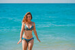 © KseniaJoyg - A young woman in a bright swimsuit and long hair walks on the sand along the sea with waves, clear azure water