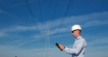 Wall Mural - the power engineer works on a tablet, standing against the background of a high-voltage power line a