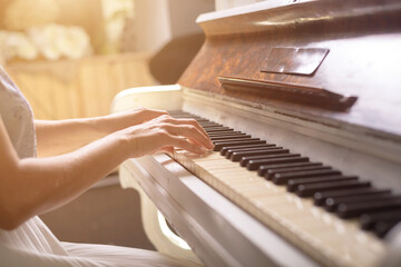 Female hands behind the keys of a white piano