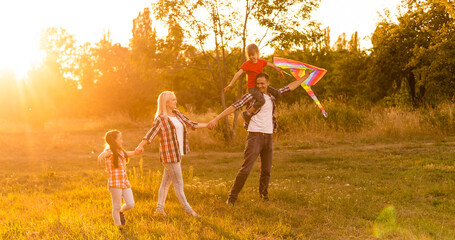 Wall Mural - Happy family with a kite playing at sunset in the field