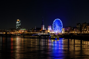 Wall Mural - Night scenery on promenade and cityscape along riverside of Rhine river and background of Ferris wheel of Christmas market festival, Weihnachtsmarkt, in Düsseldorf, Germany.