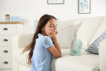 Wall Mural - Little girl enjoying air flow from portable fan at home. Summer heat