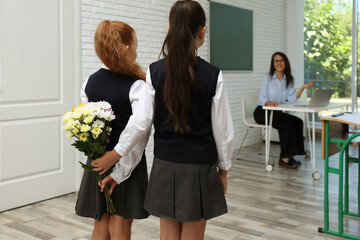 Wall Mural - Schoolgirls with bouquet congratulating their pedagogue in classroom. Teacher's day