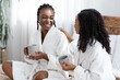 © Prostock-studio - Two young women in bathrobes sitting on bed, drinking coffee