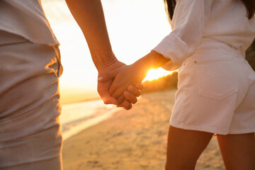 Wall Mural - Lovely couple holding hands on beach at sunset, closeup