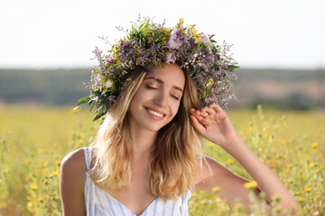 Wall Mural - Young woman wearing wreath made of beautiful flowers in field on sunny day