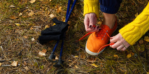 Wall Mural - Sporty hiking woman tying shoelaces on her jogging shoes while taking a break after hiking in autumn forest. hiking concept, outdoor lifestyle.