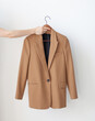 © iKagadiy - A hand holds a classic beige jacket on a wooden hanger. Dress code in the office