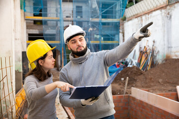 Wall Mural - Two confident engineers discussing blueprint while standing at construction site