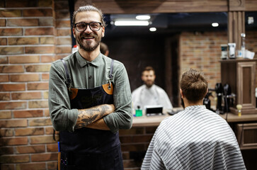 Portrait of happy young barber with client at barbershop and smiling.