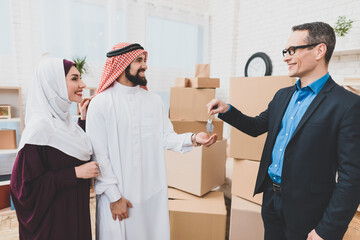 Realtor in a suit gives keys to people and smiles.