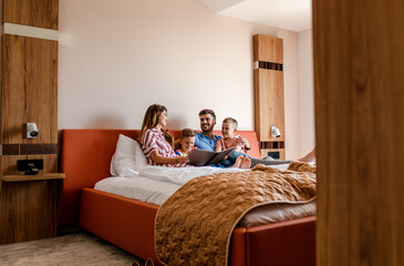 Wall Mural - family of four enjoying together at hotel room, sitting at bed reading hotels offers.