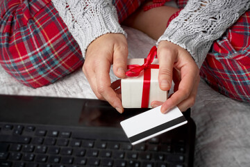 Woman in Christmas pajams buys gifts online. Human hands with credit cart and laptop. Shopping online and black friday consept.