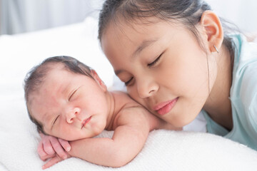 Wall Mural - little sister hugging her newborn brother. toddler kid meeting new sibling. love, trust and tenderness. cute girl and new born baby boy relax in a white bedroom. family with children at home.