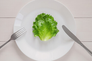 leaf lettuce on white plate with fork and knife, top view