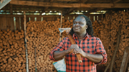 African man with the axe standing in front of stack of cutted timber for winter. High quality photo