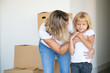 Mom and pretty little daughter moving into new flat, standing near stack of boxes and hugging. Real estate purchase concept