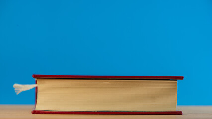 Wall Mural - One closed book lies on a blue background on an oak table.