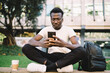© BullRun - Black man messaging on cellphone and sitting on curb