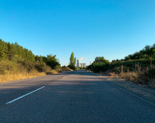 Two lanes country road at sunset leading to thermal power plant in distant