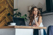 © undrey - Portrait of young woman looking at camera, sitting at the table with laptop at home