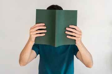 Man covering his face with a open green book.