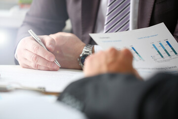 Male arm in suit and tie fill form clipped pad with silver pen closeup. Sign gesture read pact sale agent bank job make note loan credit mortgage investment finance executive chief legal teamwork law