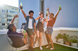 © Trevor Adeline/Caia Image - Happy young friends cheering and drinking beer on urban rooftop