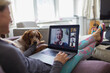 © Paul Bradbury/Caia Image - Woman with laptop video chatting with friends on sofa with dog