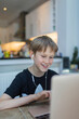 © Paul Bradbury/Caia Image - Smiling boy with headphones homeschooling at laptop