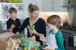 © Paul Bradbury/Caia Image - Happy mother and sons unloading fresh produce from box in kitchen