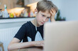 © Paul Bradbury/Caia Image - Focused boy with headphones using laptop in kitchen