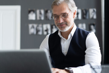 Canvas Print - Concentrated at work. Happy mature man in full suit using laptop while working in modern office